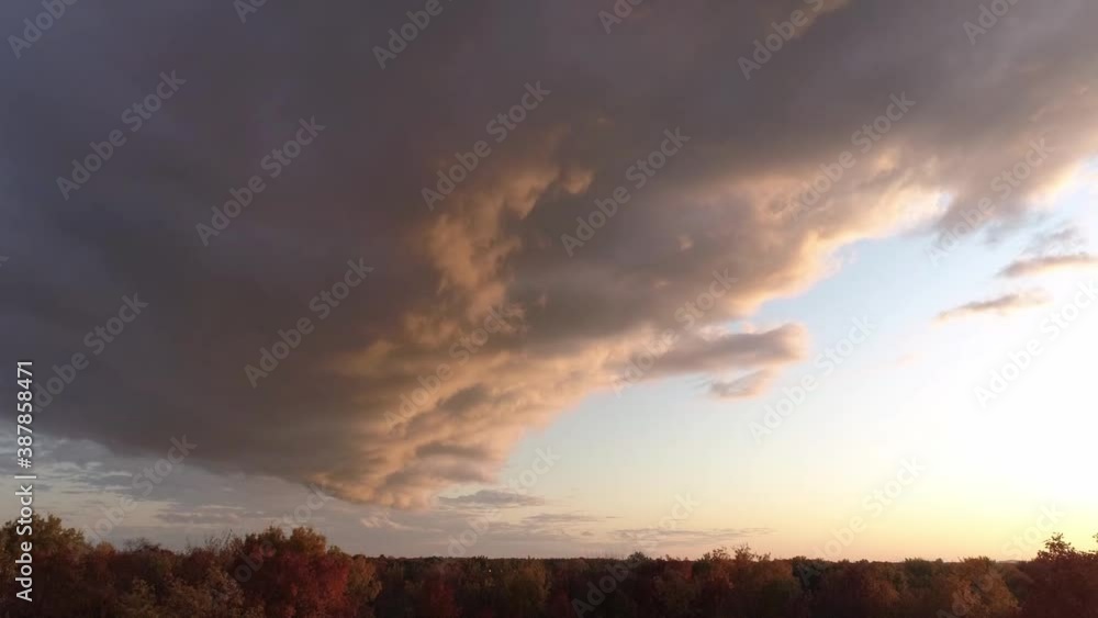 Slowly rising above the colorful trees in Autumn and showing huge clouds with the colors of a dramatic sunset