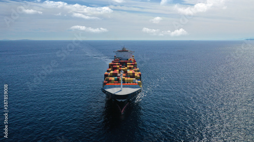 Aerial drone photo of huge container tanker ship carrying truck size colourful containers in deep blue open ocean sea