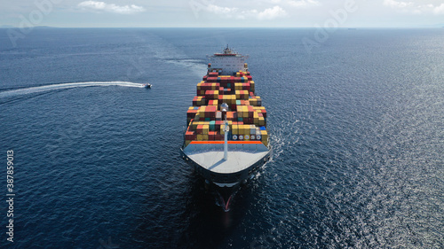 Aerial drone photo of huge container tanker ship carrying truck size colourful containers in deep blue open ocean sea