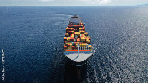 Aerial drone photo of huge container tanker ship carrying truck size colourful containers in deep blue open ocean sea
