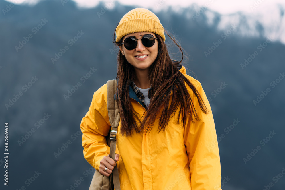 A young woman in Hiking gear stands against the backdrop of mountains and looks at the camera. A woman among the mountains. Traveling woman with a backpack on the background of mountains. Copy space A young woman in Hiking gear stands against the backdrop of mountains and looks at the camera. A woman among the mountains. Traveling woman with a backpack on the background of mountains. Copy space