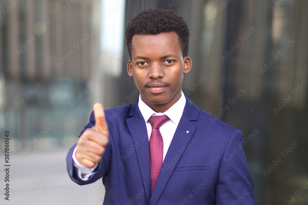 Portrait of serious handsome man, black African Afro American young businessman, office worker in formal suit with tie looking at camera, showing thumb up, like gesture. Business concept. 