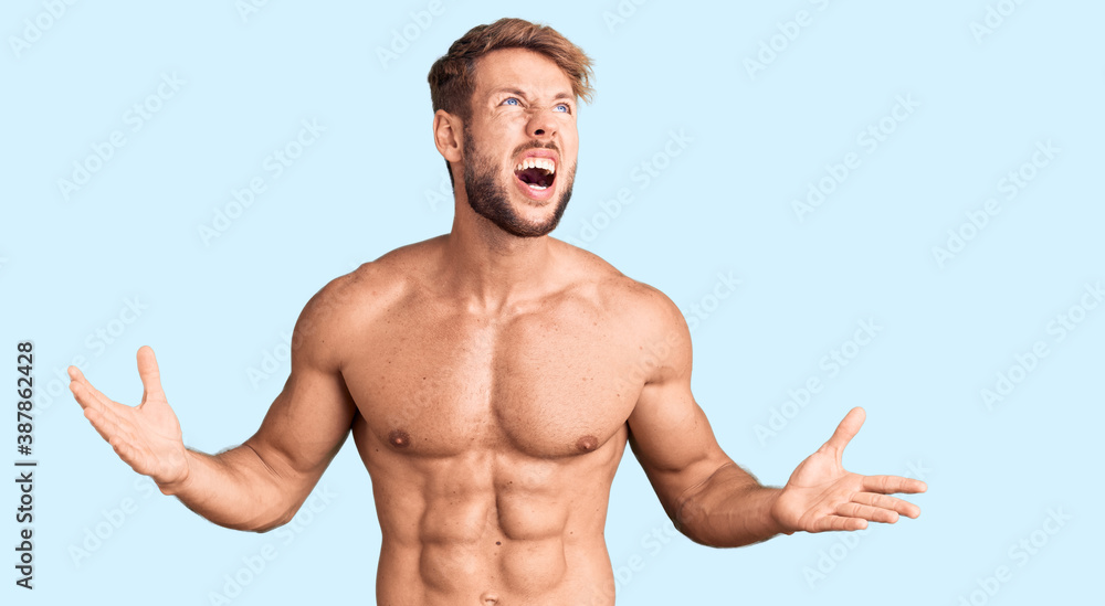 Fototapeta premium Young caucasian man standing shirtless crazy and mad shouting and yelling with aggressive expression and arms raised. frustration concept.