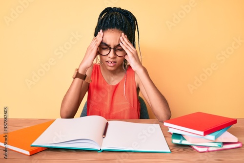 Fotografie Young african american girl child with braids studying for school exam suffering from headache desperate and stressed because pain and migraine