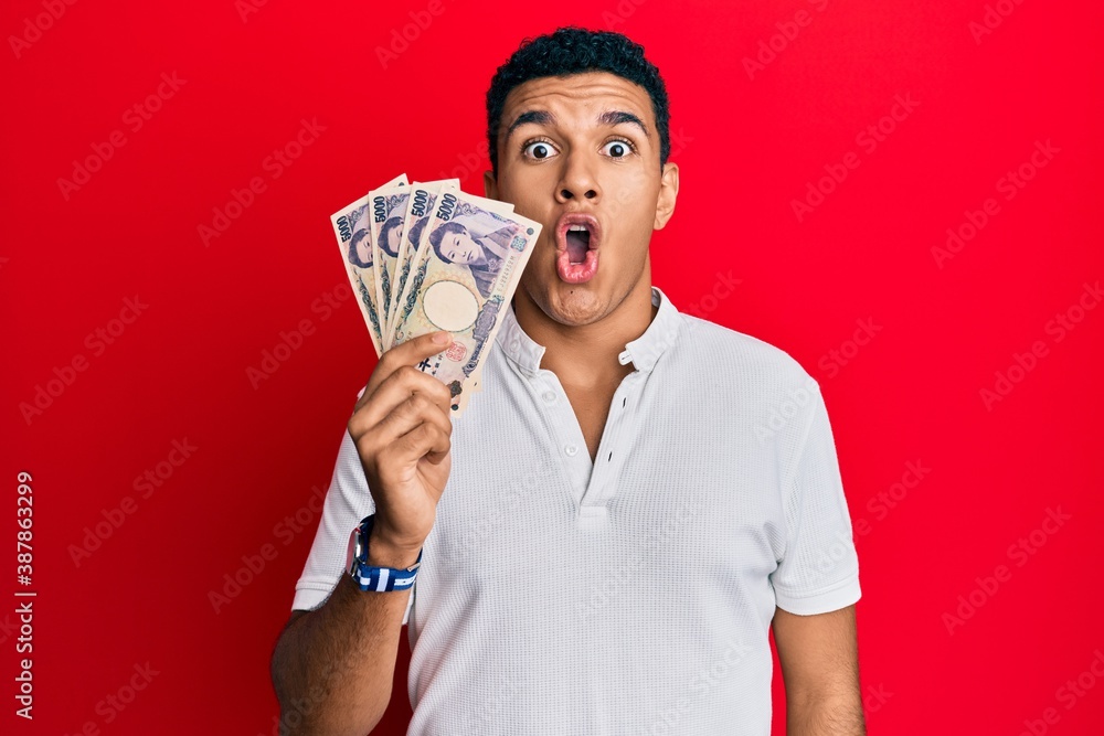 Young arab man holding japanese yen banknotes scared and amazed with open mouth for surprise, disbelief face Young arab man holding japanese yen banknotes scared and amazed with open mouth for surprise, disbelief face