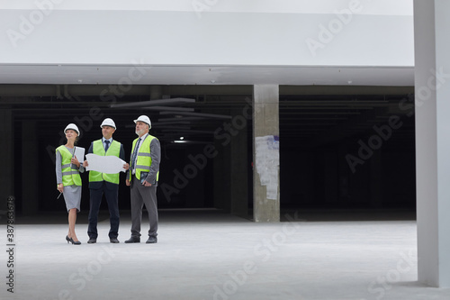 Wide angle portrait of three successful business people wearing hardhats and inspecting plans while standing at construction site indoors, copy space