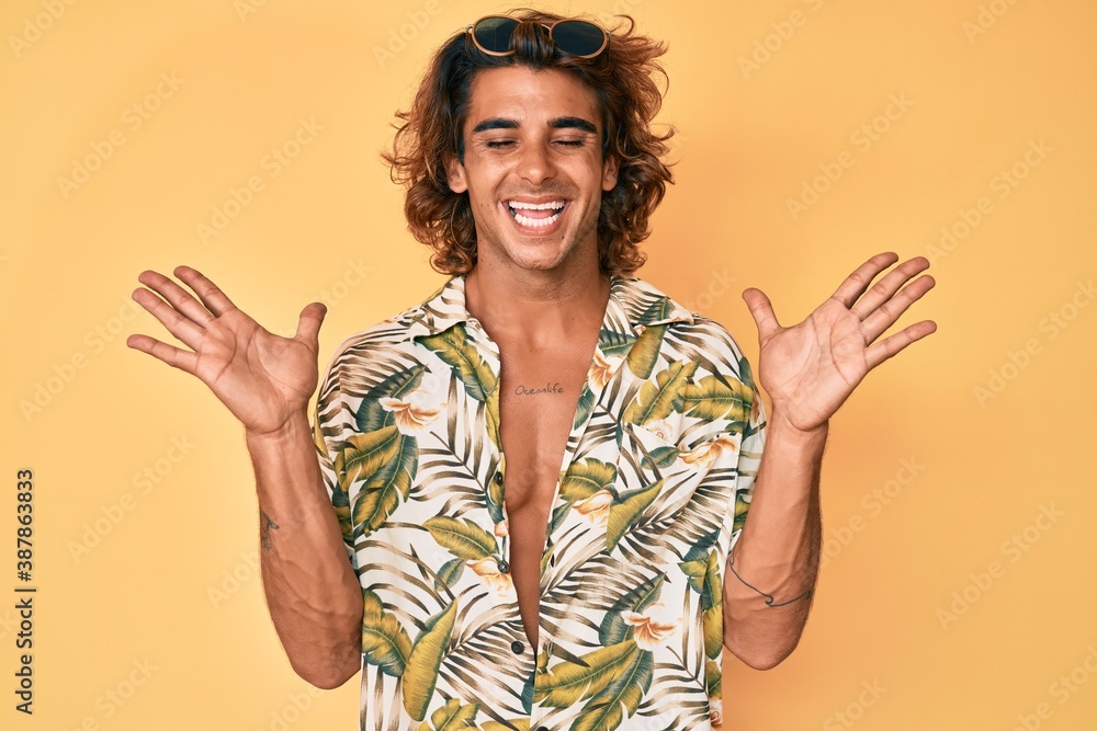 Young hispanic man wearing summer shirt celebrating mad and crazy for success with arms raised and closed eyes screaming excited. winner concept Young hispanic man wearing summer shirt celebrating mad and crazy for success with arms raised and closed eyes screaming excited. winner concept