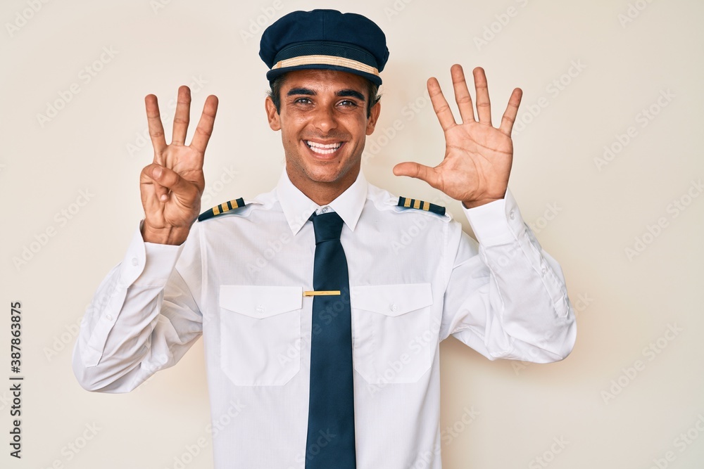 Young hispanic man wearing airplane pilot uniform showing and pointing up with fingers number eight while smiling confident and happy. Young hispanic man wearing airplane pilot uniform showing and pointing up with fingers number eight while smiling confident and happy.