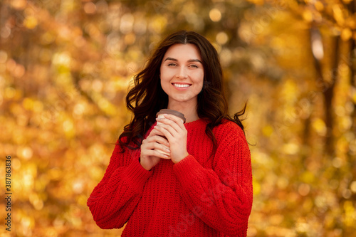 Portrait of pretty millennial lady with takeaway coffee looking at camera and smiling at beautiful autumn park