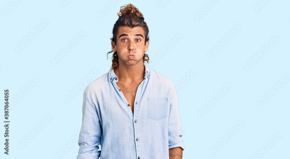 Young hispanic man wearing summer style puffing cheeks with funny face. mouth inflated with air, crazy expression. Young hispanic man wearing summer style puffing cheeks with funny face. mouth inflated with air, crazy expression.