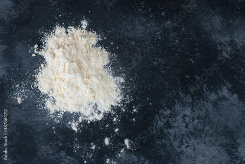 Pile of flour with a wooden shovel on a dark textured background, empty space for text