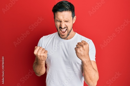 Young handsome man wearing casual white tshirt celebrating surprised and amazed for success with arms raised and eyes closed