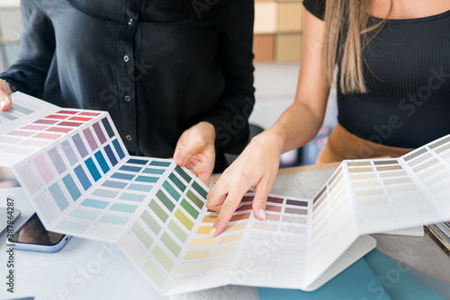 
Close-up of two women choosing samples of wall paint. Interior designer consulting a client looking at a color swatch