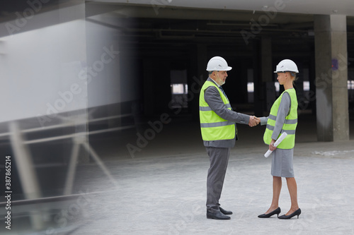 Side view portrait of smiling businessman shaking hands with female partner after investment deal at construction site, copy space