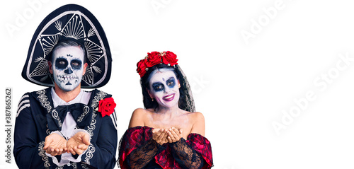 Young couple wearing mexican day of the dead costume over background smiling with hands palms together receiving or giving gesture. hold and protection