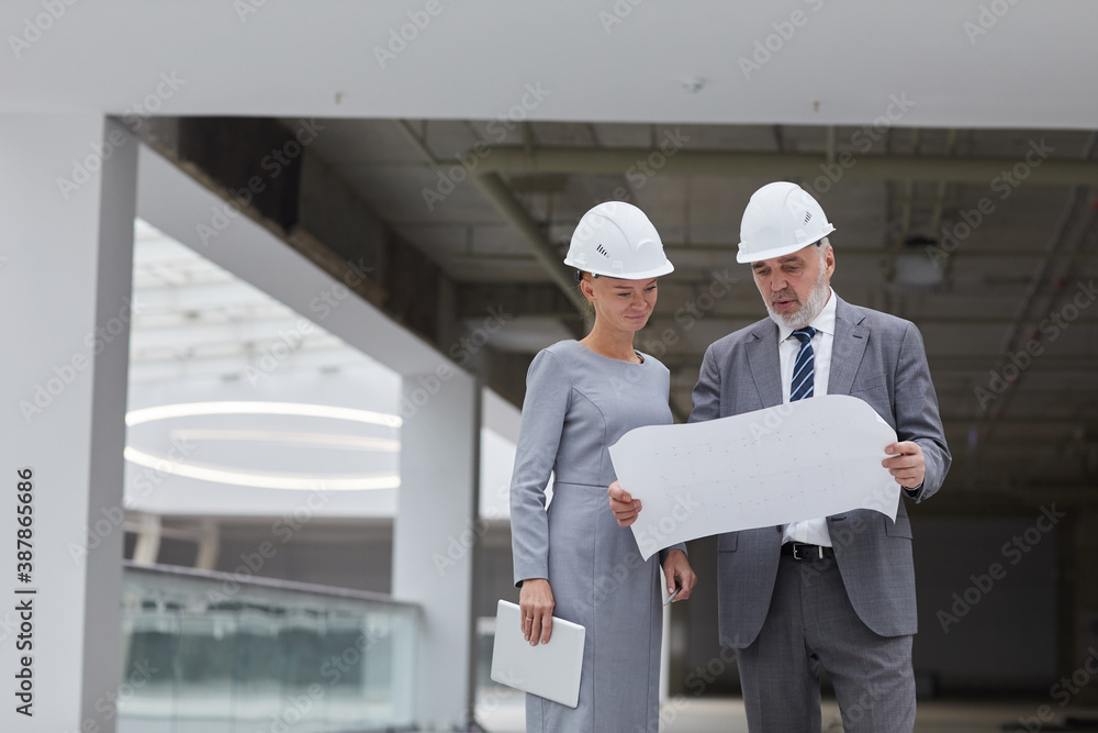 Waist up portrait of smiling businesswoman looking at plans at construction site indoors, copy space Waist up portrait of smiling businesswoman looking at plans at construction site indoors, copy space