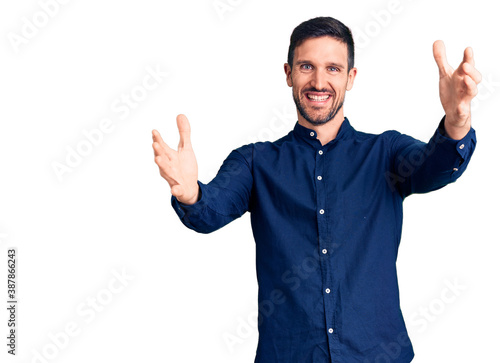 Young handsome man wearing casual shirt looking at the camera smiling with open arms for hug. cheerful expression embracing happiness.