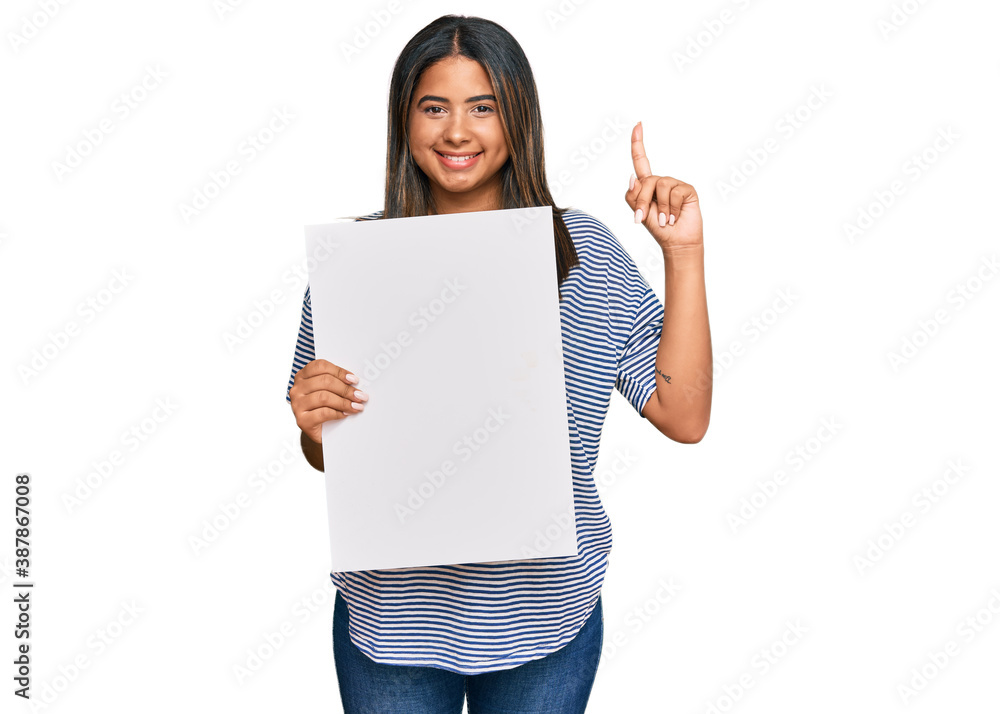 Young latin girl holding blank empty banner surprised with an idea or question pointing finger with happy face, number one Young latin girl holding blank empty banner surprised with an idea or question pointing finger with happy face, number one