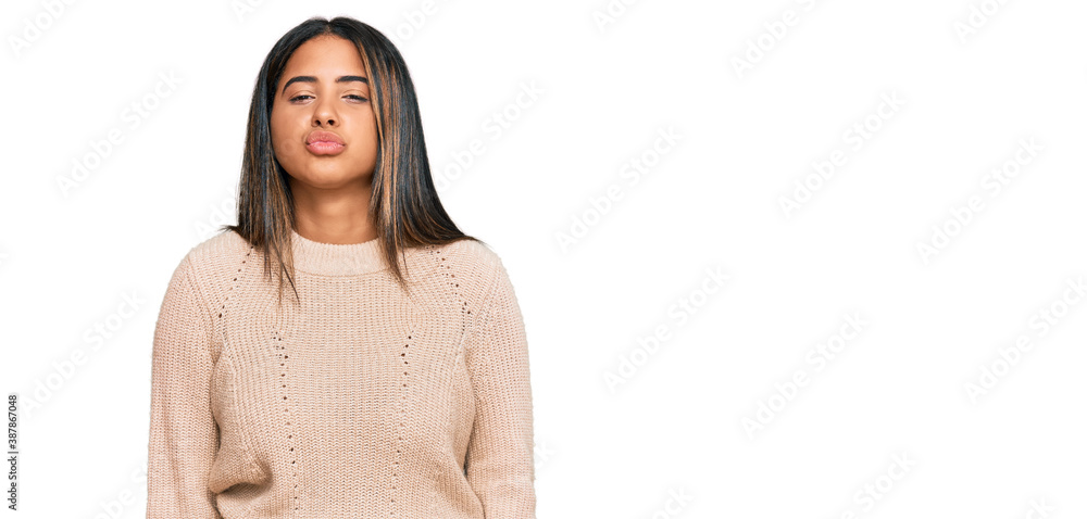 Young latin girl wearing wool winter sweater looking at the camera blowing a kiss on air being lovely and sexy. love expression. Young latin girl wearing wool winter sweater looking at the camera blowing a kiss on air being lovely and sexy. love expression.
