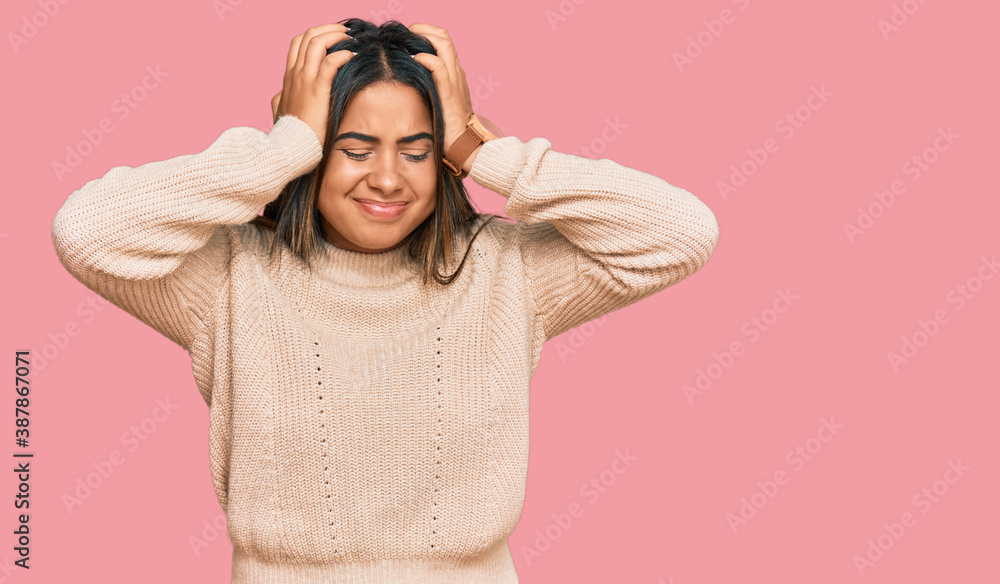 Young latin girl wearing wool winter sweater suffering from headache desperate and stressed because pain and migraine. hands on head. Young latin girl wearing wool winter sweater suffering from headache desperate and stressed because pain and migraine. hands on head.
