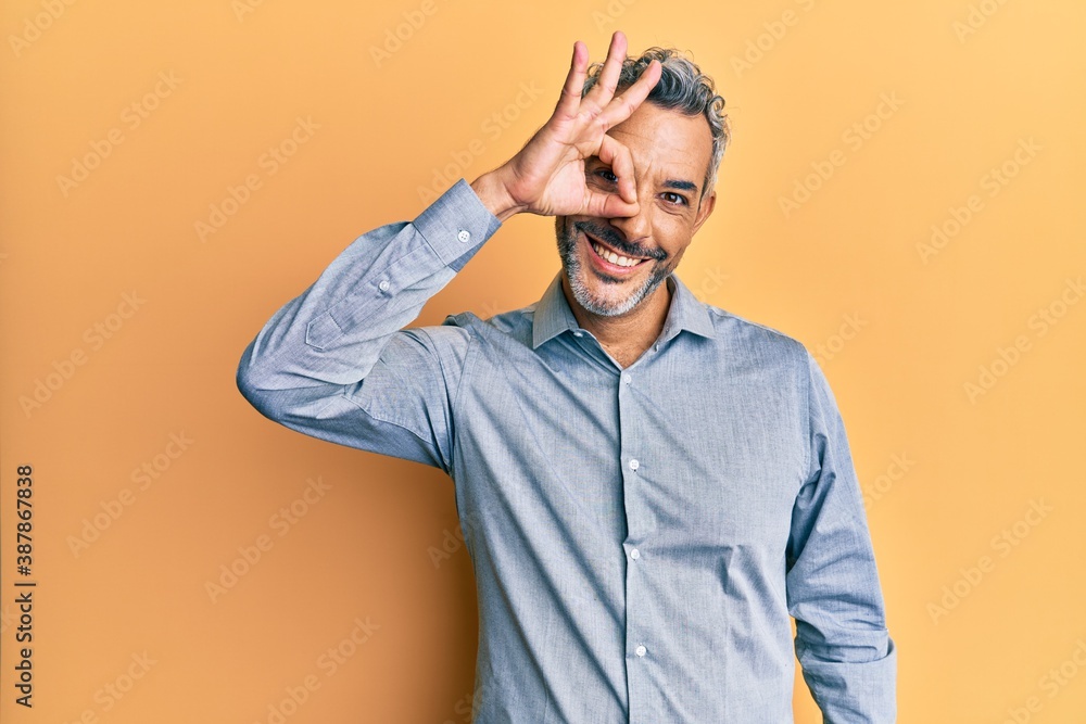 Middle age grey-haired man wearing casual clothes smiling happy doing ok sign with hand on eye looking through fingers