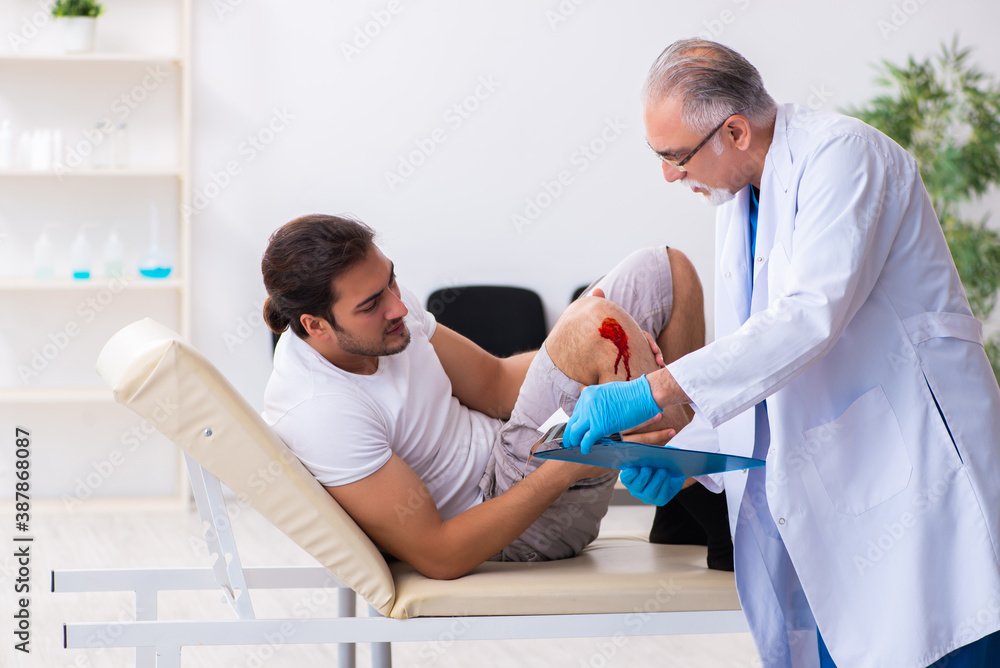 Fototapeta premium Leg injured man visiting old doctor in first aid concept