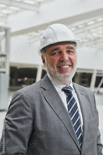 Vertical portrait of smiling senior businessman wearing hardhat and looking at camera while standing at construction site