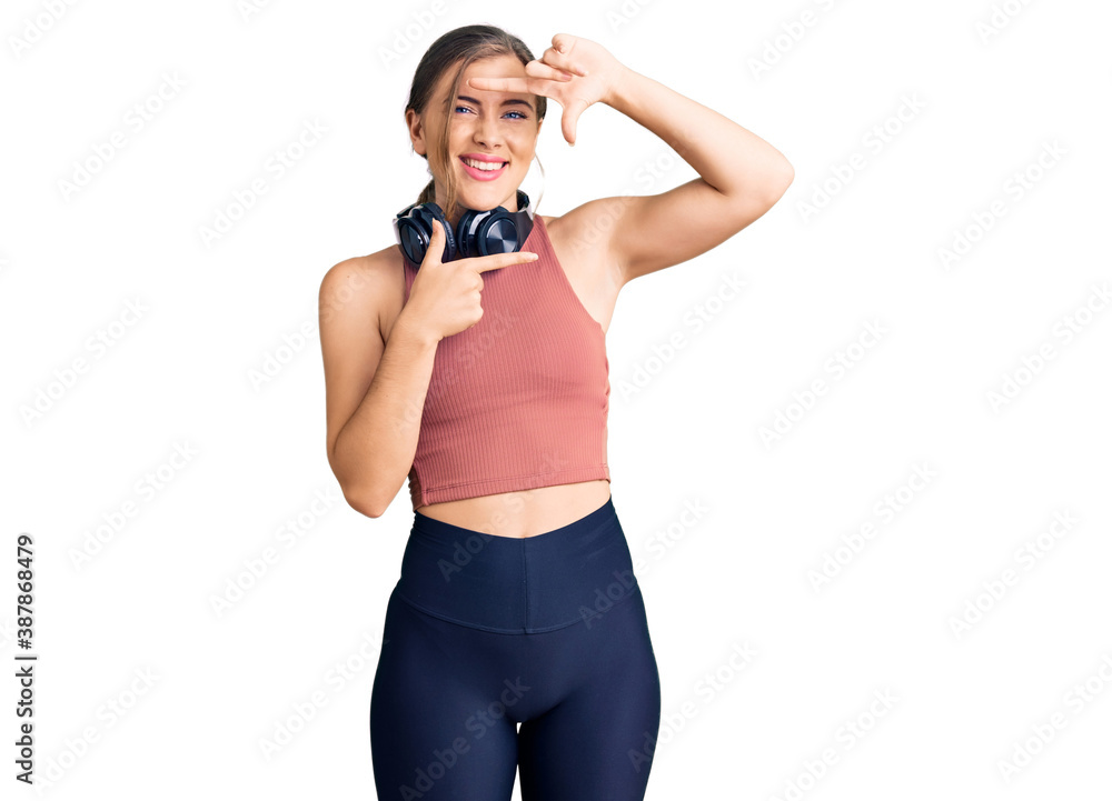 Beautiful caucasian young woman wearing gym clothes and using headphones smiling making frame with hands and fingers with happy face. creativity and photography concept. Beautiful caucasian young woman wearing gym clothes and using headphones smiling making frame with hands and fingers with happy face. creativity and photography concept.
