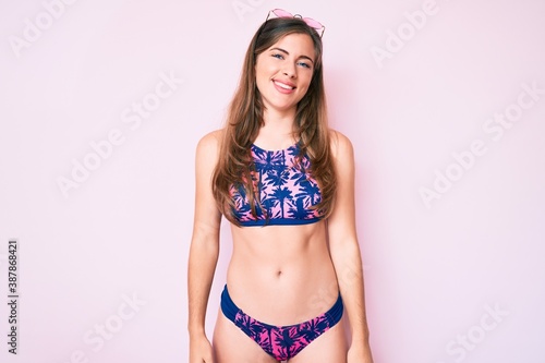 Beautiful young caucasian woman wearing bikini and sunglasses looking away to side with smile on face, natural expression. laughing confident.