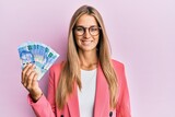 Young blonde woman wearing business style holding south african rands banknotes looking positive and happy standing and smiling with a confident smile showing teeth