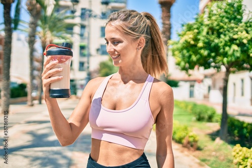 Young blonde sporty girl smiling happy drinking healthy protein smoothie at street of city.