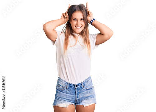 Beautiful caucasian woman wearing casual white tshirt posing funny and crazy with fingers on head as bunny ears, smiling cheerful