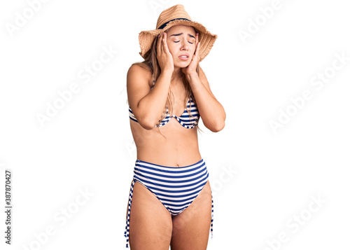 Young beautiful blonde woman wearing bikini and hat with hand on head, headache because stress. suffering migraine.