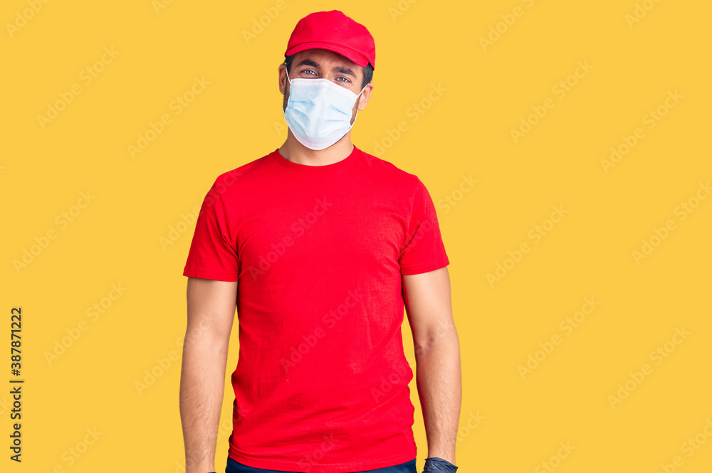 Young hispanic man wearing covid-19 safety mask looking positive and happy standing and smiling with a confident smile showing teeth Young hispanic man wearing covid-19 safety mask looking positive and happy standing and smiling with a confident smile showing teeth