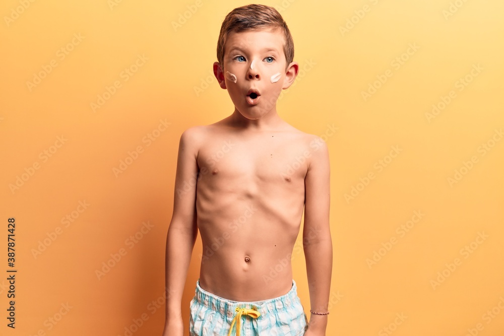 Cute blond kid wearing swimwear scared and amazed with open mouth for surprise, disbelief face