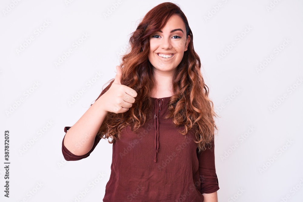 Young beautiful woman wearing casual clothes smiling happy and positive, thumb up doing excellent and approval sign Young beautiful woman wearing casual clothes smiling happy and positive, thumb up doing excellent and approval sign