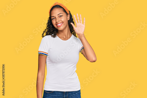 Young african american girl wearing casual clothes waiving saying hello happy and smiling, friendly welcome gesture