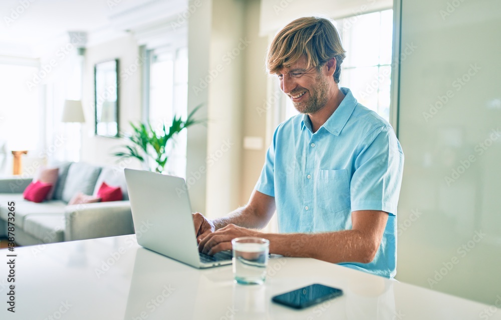 Young irish man smiling happy working using laptop sitting on the table at home.
