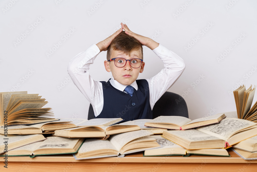 Education concept. The student does his homework, holds his head with his hands and looks at the camera. There are many open books on the table. Education concept. The student does his homework, holds his head with his hands and looks at the camera. There are many open books on the table.