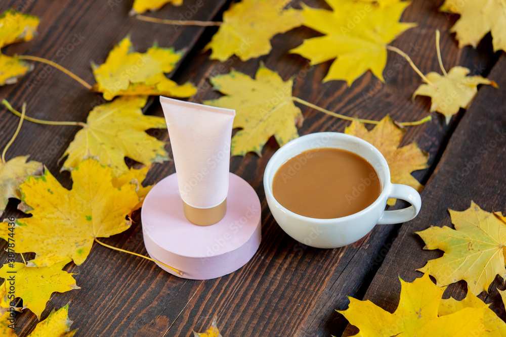 Φωτογραφία Cup of coffee and cream tube next to yellow maple leaves on a green grass