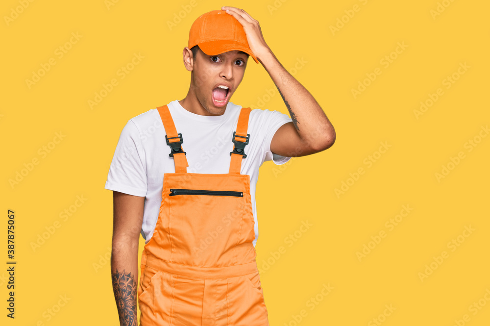 Young handsome african american man wearing handyman uniform surprised with hand on head for mistake, remember error. forgot, bad memory concept.