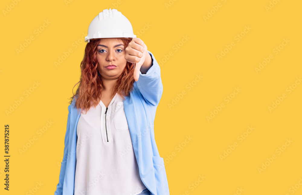 Young latin woman wearing architect hardhat looking unhappy and angry showing rejection and negative with thumbs down gesture. bad expression. Young latin woman wearing architect hardhat looking unhappy and angry showing rejection and negative with thumbs down gesture. bad expression.