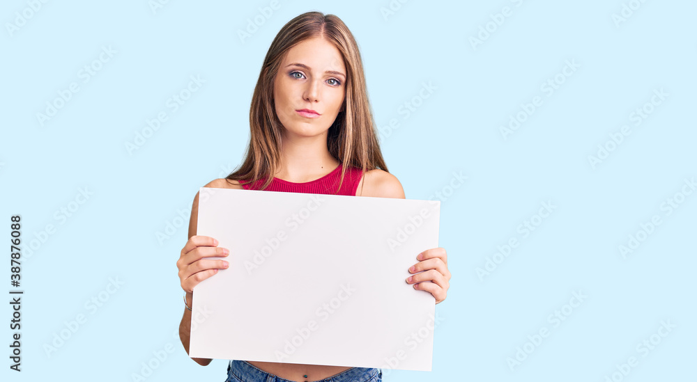 Young beautiful blonde woman holding blank empty banner thinking attitude and sober expression looking self confident Young beautiful blonde woman holding blank empty banner thinking attitude and sober expression looking self confident