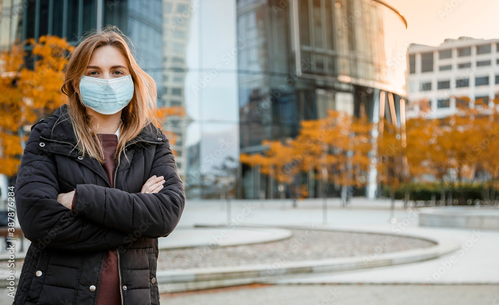Girl in a mask near the house. Woman in medical mask outdoors in autumn. Epidemic in the fall. Protection against COVID-19.
