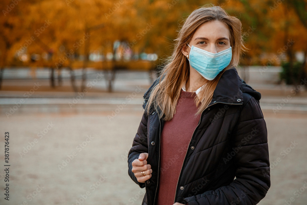 Girl in a mask near the house. Woman in medical mask outdoors in autumn. Epidemic in the fall. Protection against COVID-19. Girl in a mask near the house. Woman in medical mask outdoors in autumn. Epidemic in the fall. Protection against COVID-19.