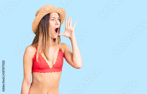 Beautiful brunette young woman wearing bikini shouting and screaming loud to side with hand on mouth. communication concept.
