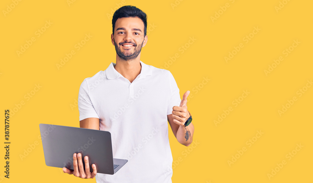 Young handsome hispanic man working using computer laptop smiling happy and positive, thumb up doing excellent and approval sign Young handsome hispanic man working using computer laptop smiling happy and positive, thumb up doing excellent and approval sign