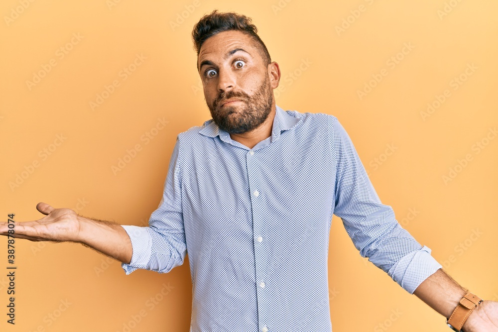 Handsome man with beard wearing casual clothes clueless and confused expression with arms and hands raised. doubt concept. Handsome man with beard wearing casual clothes clueless and confused expression with arms and hands raised. doubt concept.