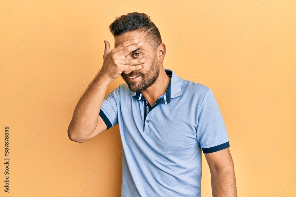 Handsome man with beard wearing casual clothes peeking in shock covering face and eyes with hand, looking through fingers with embarrassed expression. Handsome man with beard wearing casual clothes peeking in shock covering face and eyes with hand, looking through fingers with embarrassed expression.