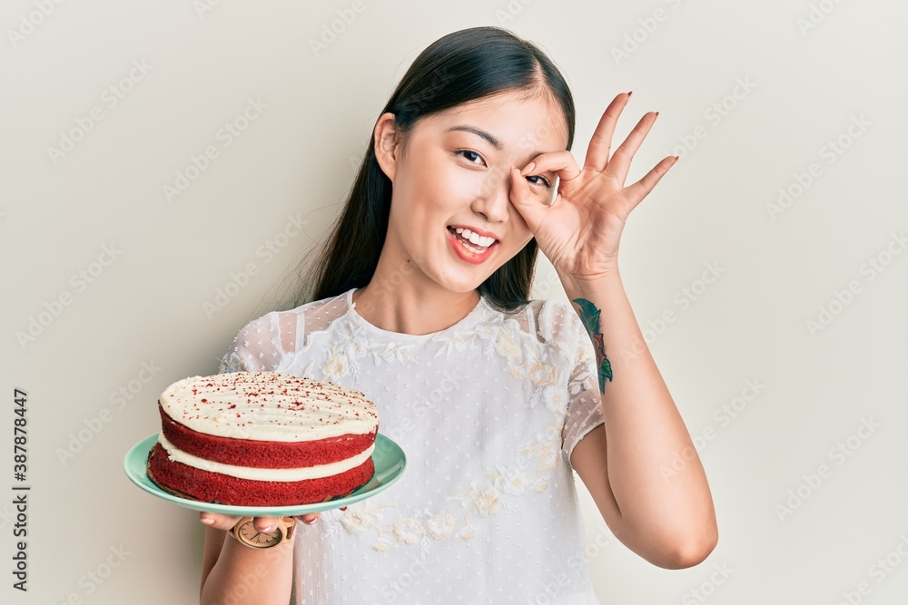 Young chinese woman holding carrot cake smiling happy doing ok sign with hand on eye looking through fingers Young chinese woman holding carrot cake smiling happy doing ok sign with hand on eye looking through fingers